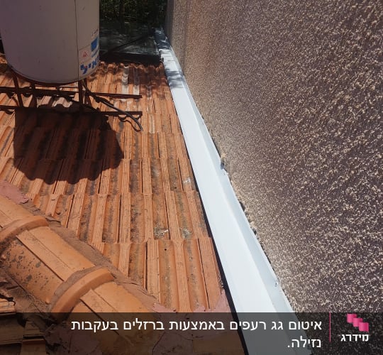 רעפים חומים על גג עם מרזב לבן צמוד לקיר
